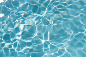 Blue water with ripples on the surface. Defocus blurred transparent blue colored clear calm water surface texture with splashes and bubbles. Water waves with shining pattern texture background.