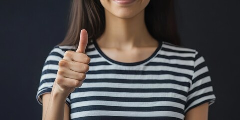 Unrecognizable female figure in a striped sailor t shirt giving a thumbs up gesture, expressing recognition and approval. This image captures a sense of positivity and affirmation through the gesture.