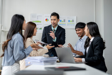 A group of people are sitting around a table with a laptop and papers