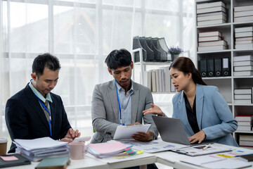 Three people in suits are sitting at a desk with a laptop open