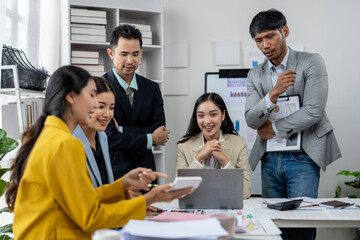 A group of people are gathered around a table with a laptop and a tablet