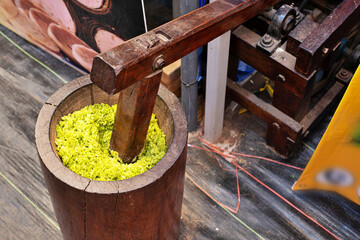 A wooden barrel with a green substance inside. The barrel is sitting on a wooden table. The barrel is full of green stuff