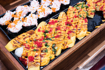 A tray of sushi with a yellow sauce and red garnish. The sushi is arranged in a way that makes it look appetizing and inviting