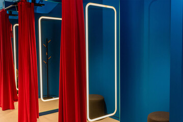 Fitting room in stylish clothing store, dressroom red curtains and large mirror
