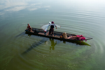 Fisherman casting his net at sunrise. Silhouette Asian fisherman on wooden boat casting a net in the Lake. Vietnamese Fisherman throwing net.