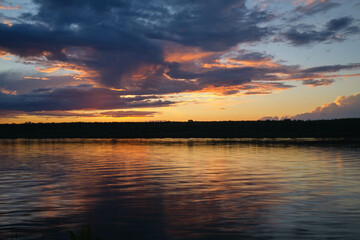 Colorful summer sunset on the river bank. Natural landscape. Reflection, blue sky and yellow sunlight. Landscape during sunset