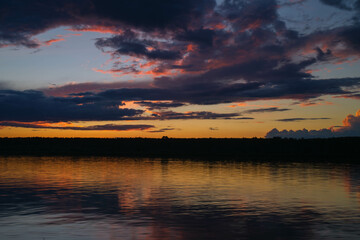 Colorful summer sunset on the river bank. Natural landscape. Reflection, blue sky and yellow sunlight. Landscape during sunset