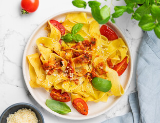 Flat lay of tagliatelle or pappardelle pasta with tomato sauce, basil and parmesan cheese in a plate on a marble background