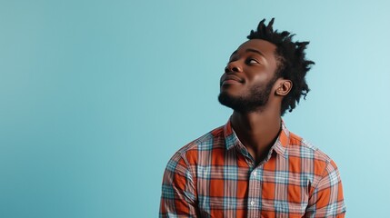 Fototapeta premium Young man in a plaid shirt looking up against a blue background
