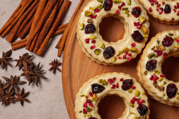 Festive ring-shaped cookies topped with icing, pistachios, and dried fruits, flat lay.