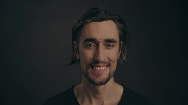 Cheerful Young European Guy Smiling Young attractive European man with big eyes and dimples waves hello with a bright smile and a humorous expression.
