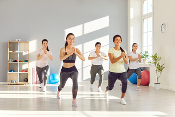 Group of fit and active female group doing sport exercises in gym. Happy smiling women in sportswear having workout indoors together. Sport training, exercising and fitness concept.