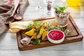 Potatoes wedges with salted herring on wooden board