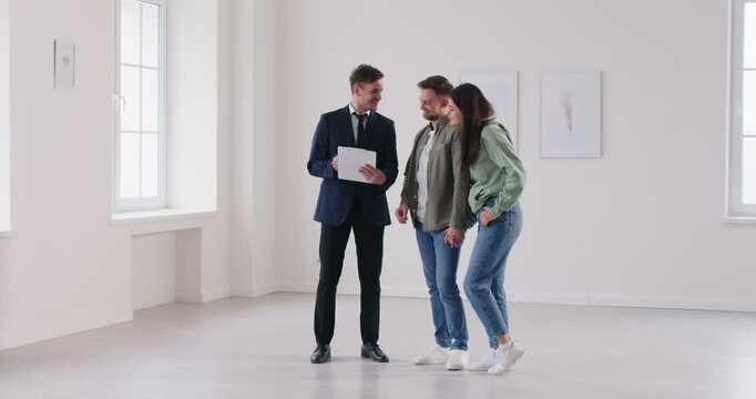 Young couple, small family, realtor in empty room watching papers, flat documentation. Helping clients buy, rent home, apartment, real estate agent advertising, assisting buyers, display real property