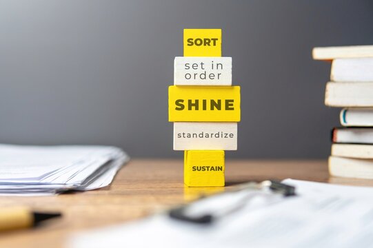 The 5s workplace organization method. Stack of wooden tiles with text SORT, SET IN ORDER, SHINE, STANDARDIZE and SUSTAIN.