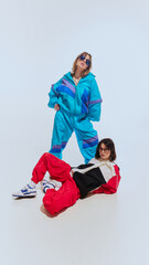 Two women in 90s-inspired style, eyewear, windbreakers and vibrant tracksuits, posing together...