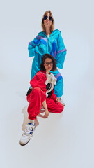Two women in 90s-inspired style, eyewear, windbreakers and vibrant tracksuits, posing together...