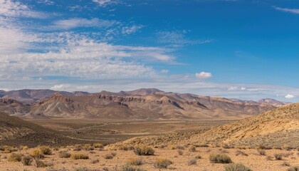 Fototapeta premium Vast desert landscape with mountains under a bright blue sky and scattered clouds. Nature and wilderness concept