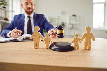 Young male judge working in office with wooden human toy figures of family with two kids are...