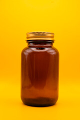 Amber glass jar with golden lid on vibrant yellow background