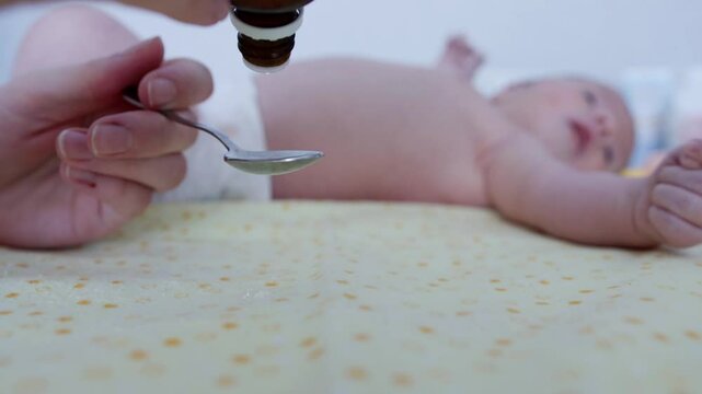 medicinal medical drops in a spoon against the background of a newborn baby for colic in the tummy. Copy space for text