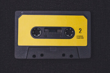 Obraz premium Retro black audio cassette with yellow label on dark textured background