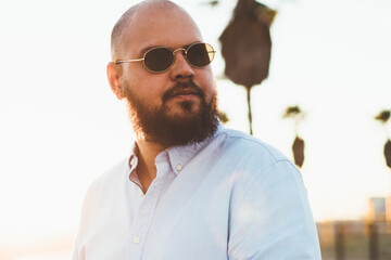 Serious hipster guy looking away standing outdoors with smartphone in hands for sending online text messages, handsome young male using modern telephone and 4G connection for networking and blogging