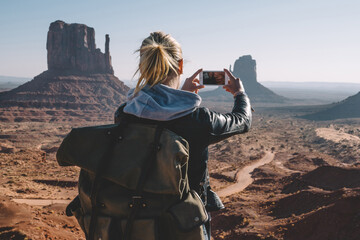 Back view of female with backpack photographing scenery landscape of Monument Valley using...