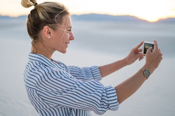 Smiling young blogger posing for selfie on smartphone standing in White Sands National park, hipster girl taking picture of scenery beautiful nature during trip enjoying wanderlust summer vacations