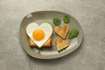 Heart shaped fried egg and toasts on grey marble table, top view