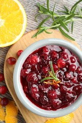 Tasty cranberry sauce in bowl, berries, orange and rosemary on wooden table, top view