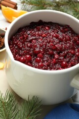 Tasty cranberry sauce in saucepan and fir branches on table, closeup