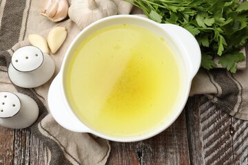 Tasty chicken bouillon in bowl and ingredients on wooden table, flat lay