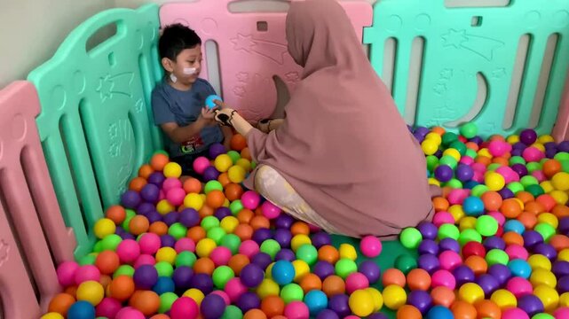 A child living with Cerebral palsy sits in a colorful ball hole when interacting with a mother in play room