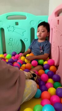 A child who lives with Cerebral palsy and wears a nasogastric tube or NGT on his nose is playing in a pool full of colorful balls