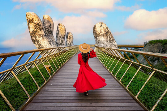 Asian woman in Vietnamese national costume on the Golden Bridge with Two Giant Hands, a viewpoint at a popular tourist attraction in Ba Na Hills Resort, Danang, Vietnam.
