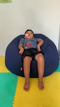 Children who use NGT (nasogastric tube) or a probe on their nose are sleepy while sitting on a blue bean-shaped sofa