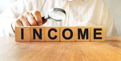 INCOME inscription on the texture of wooden cubes. A business man holds a cube in his hand. An inscription on a financial, business or economic theme.