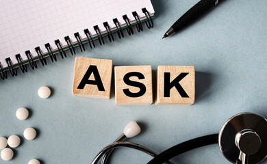 Wooden cubes with the inscription ASK lie on the table. View from above. Nearby is a stethoscope, a notebook and scattered pills.
