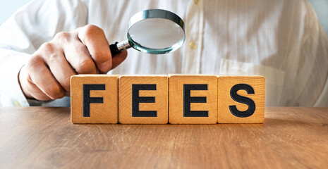 FEES inscription on the texture of wooden cubes. A business man holds a cube in his hand. An inscription on a financial, business or economic theme.