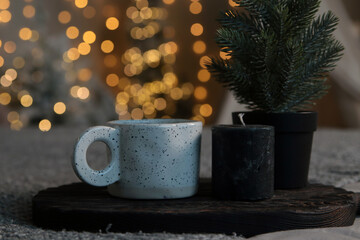 New Year interior. White cup, candle and small Christmas tree in a pot on a blurred bokeh background. Close-up. Copyspace
