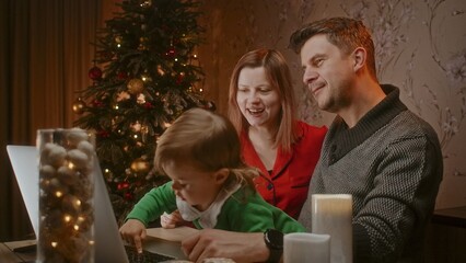 Happy family with cute small kid child daughter using laptop with Christmas tree having virtual party dinner on video call.