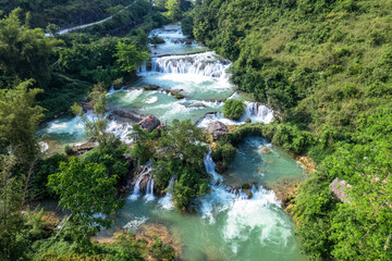 Lush forest and turquoise waterfall flowing through the valley in countryside