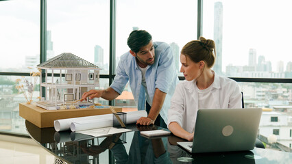 Smart architect engineer inspect house model while colleague using laptop analysis data. Professional designer team working together to design house model construction at modern office. Tracery