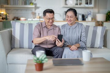 An elderly couple sits together in their cozy living room, smiling and enjoying a moment as they look at something on a smartphone. Their warmth and affection capture a peaceful home atmosphere.