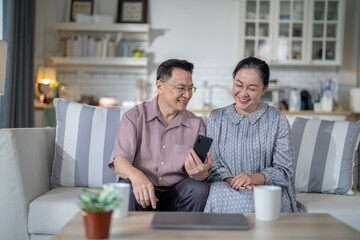 An elderly couple sits together in their cozy living room, smiling and enjoying a moment as they look at something on a smartphone. Their warmth and affection capture a peaceful home atmosphere.