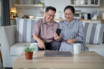 An elderly couple sits together in their cozy living room, smiling and enjoying a moment as they look at something on a smartphone. Their warmth and affection capture a peaceful home atmosphere.