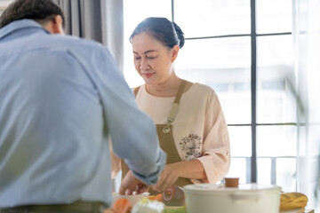 A woman prepares fresh vegetables in a cozy kitchen, while a man assists in the background. The scene emphasizes a warm and healthy lifestyle with a focus on fresh produce and home cooking.