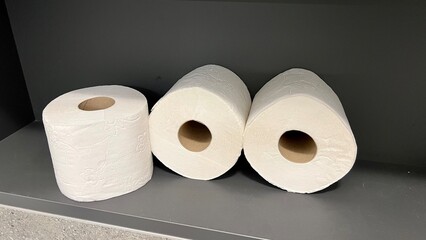 Horizontal photo of toilet paper rolls lying randomly on a shelf in the bathroom. The rolls are placed on a dark background, highlighting their texture and everyday use.