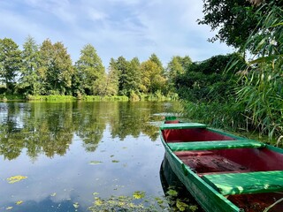 Wooden boat on the riverbank near the lake shore, set against a background of trees and reeds. Captures a tranquil waterside scene with natural elements and rustic charm